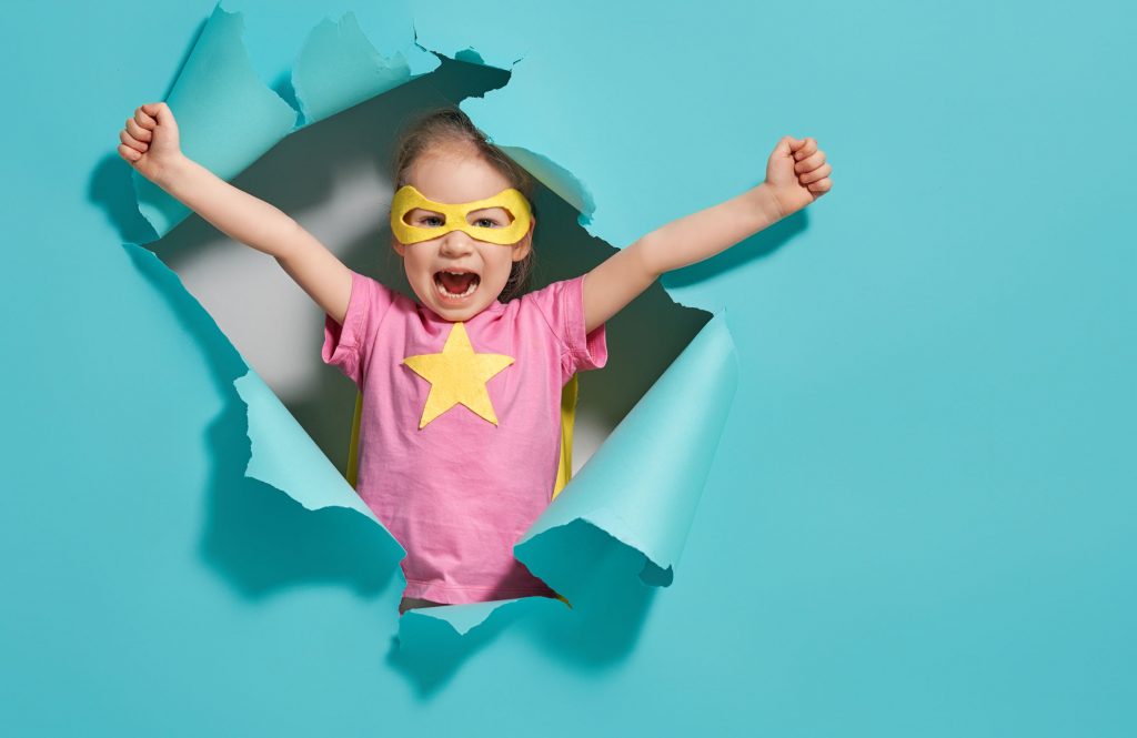 Girl in superhero costume bursting out from a paper wall